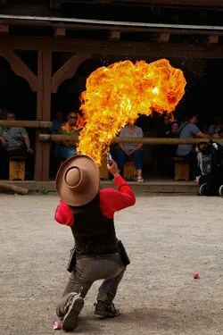 Man with a cowboy outfit kneels and breaths fire.