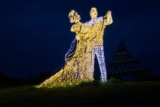 Light sculpture of two people dancing at night. Cone building in the background.