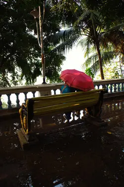 A couple with a red umbrella sits on a bench.