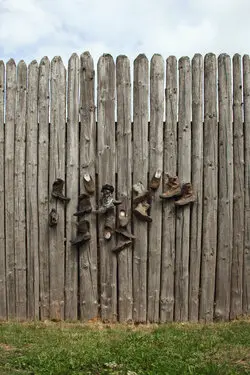 Shoes hanging on a tall wooden fence.