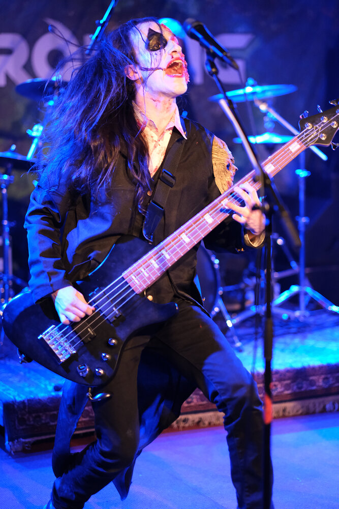 Bass player with a white-painted face covered by fake blood and skin.