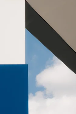 An abstract photography. White and blue rectangles complement the sky and clouds. Diagonal gray and beige surfaces add depth to the photo.