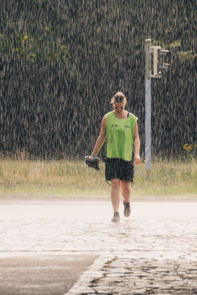 An event marshal/steward holding a rain poncho and walking through heavy rain.