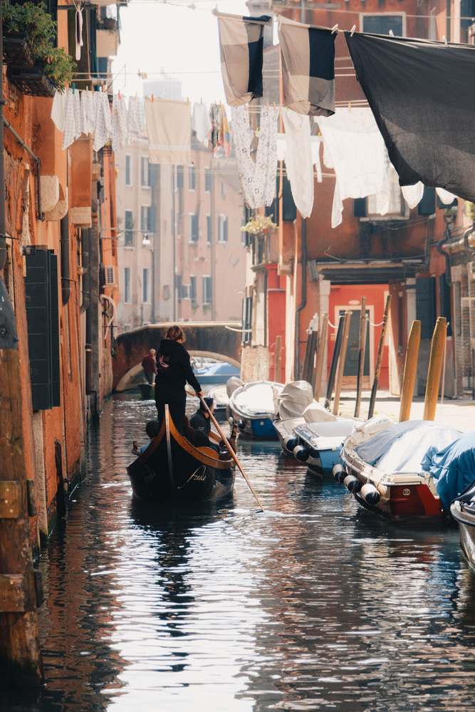 A rowing boat on a water canal, viewed from behind. Washed clothes are hanging above the canal.